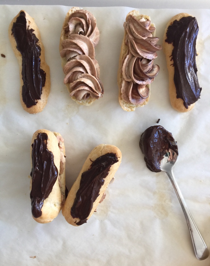 Piping the mocha cream on each eclair & spooning the chocolate on top.